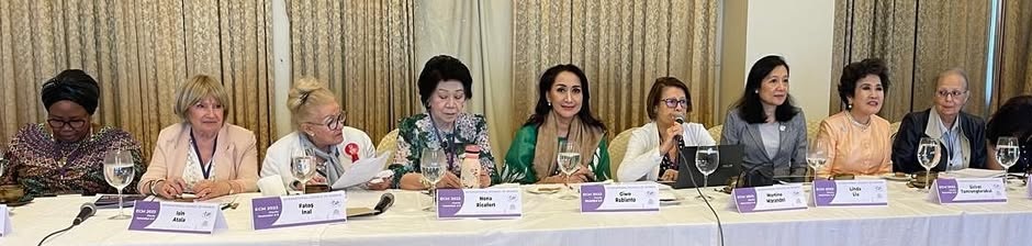 Foto Giwo Rubianto tersenyum di tengah beberapa perempuan dari berbagai negara, dengan latar belakang bendera atau simbol acara internasional, menggambarkan inspirasi dan kolaborasi global.